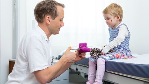 Doctor showing a little girl with epidermolysis bullosa how to do dressings on the childs soft toy