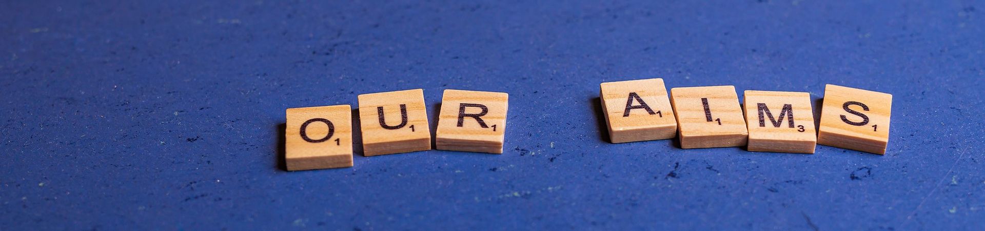 Alphabetic characters on small wooden blocks lying on a blue background, showing the words our aims