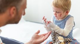 Child with EB with dressings on hands and arms sitting in front of a care taker