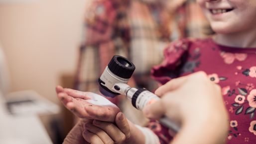 Hand of child with Epidermolysis bullosa being examined by a doctor with an reflecting microscope